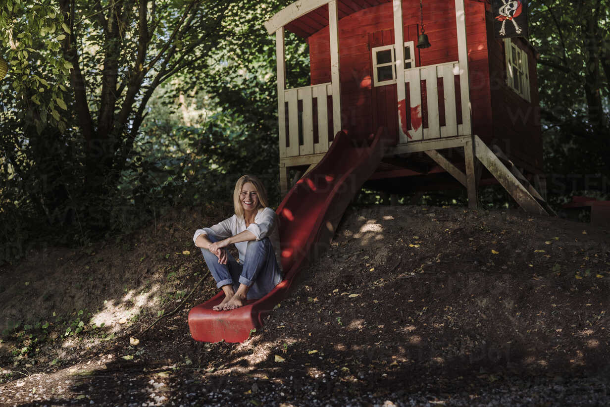 Mature Woman Sitting On Slide In Front Of Garden Shed In The Woods