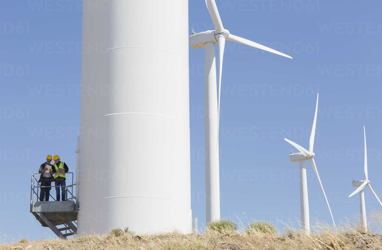 Workers talking on wind turbine in rural landscape ...