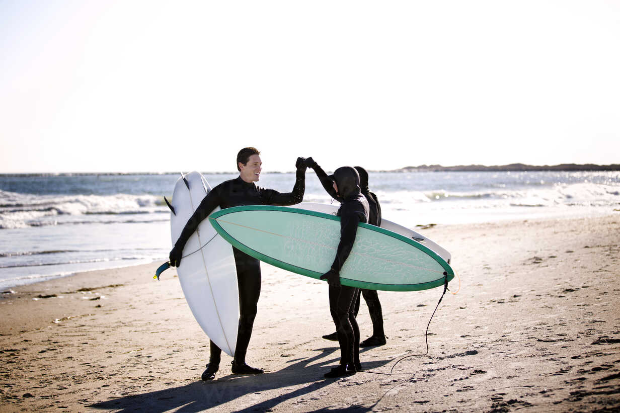 Surfers doing fist bump while standing at beach - CAVF11287 - Cavan ...