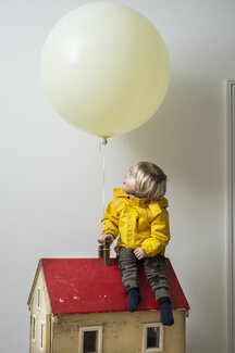 Boy Sitting On Dolls House Looking Up At Balloon Cuf David Cleveland Westend61