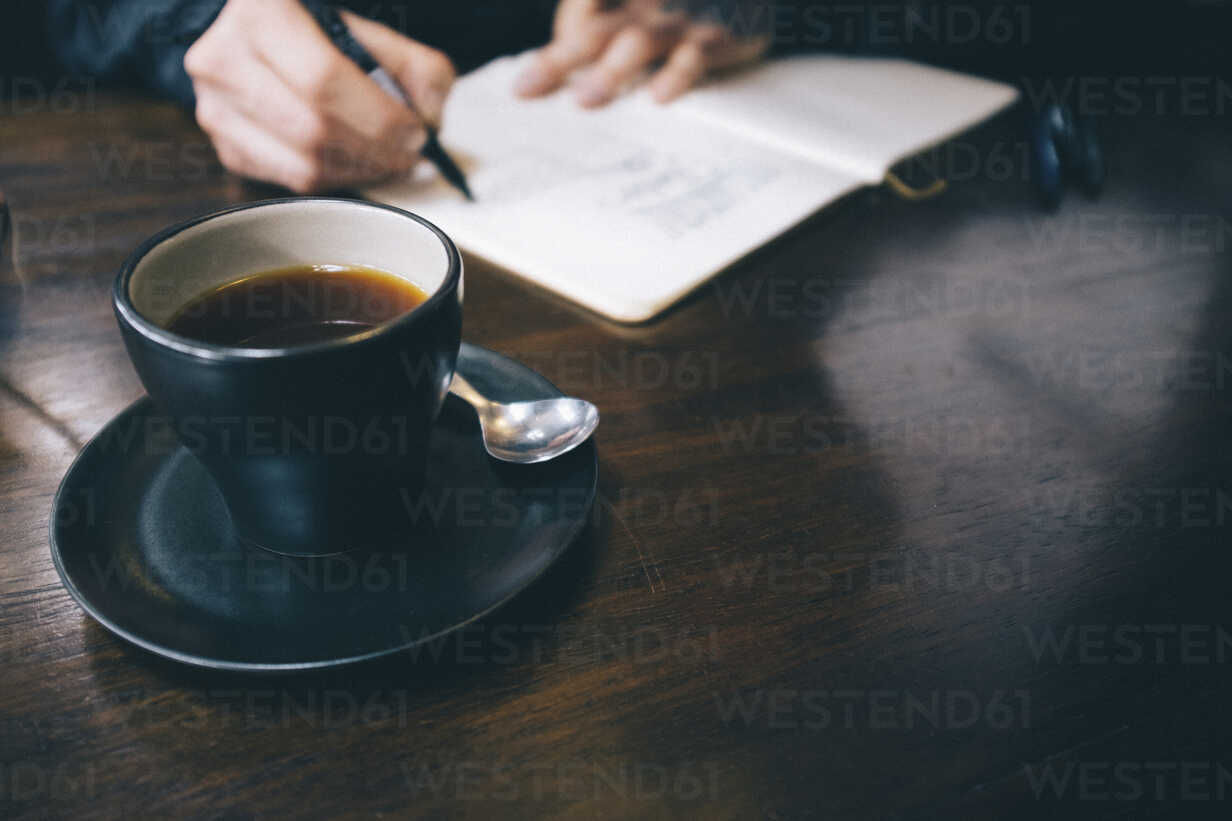 Cropped Hands Of Man Writing With Black Coffee Served On Table Stockphoto