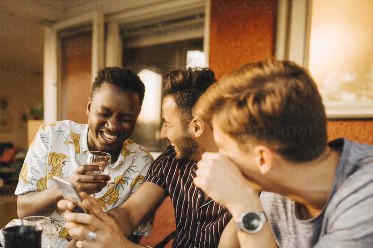 Cheerful Male Friends Using Smart Phone While Having Fun In Dinner Party Stockphoto