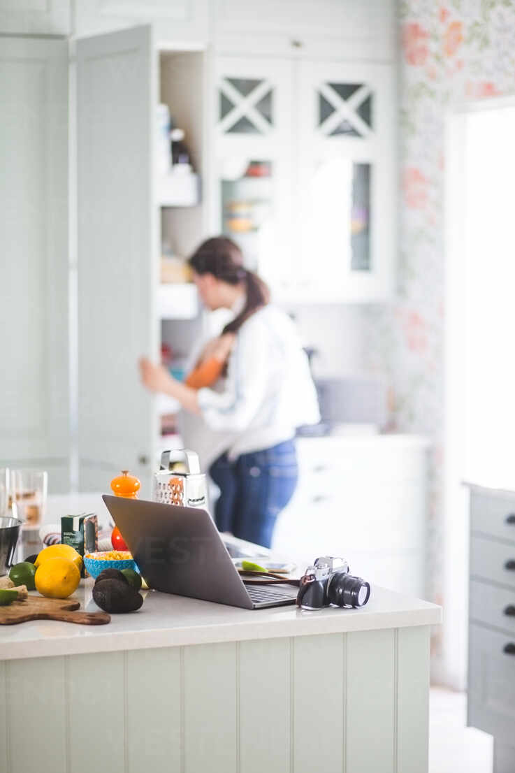 Working Mother With Daughter Preparing For Blog In Kitchen At Home Stockphoto