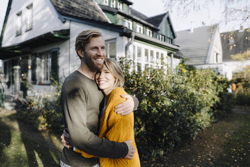 Ein glückliches Paar umarmt sich vor seinem Haus - KNSF07100