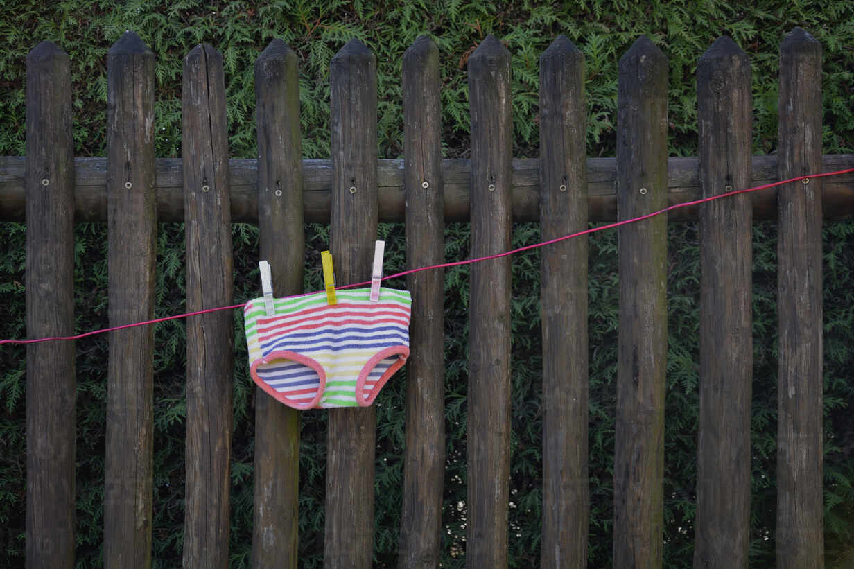 Colorful Underpants Drying On Clothesline In Front Of Wooden Fence Stockphoto