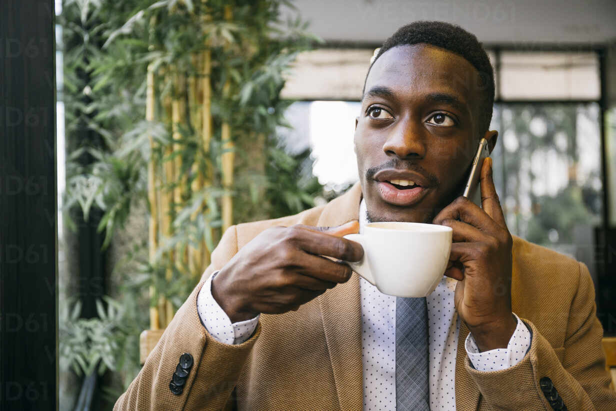 Young Businessman Drinking A Cup Of Coffee And Talking On The Phone In A Cafe Stockphoto
