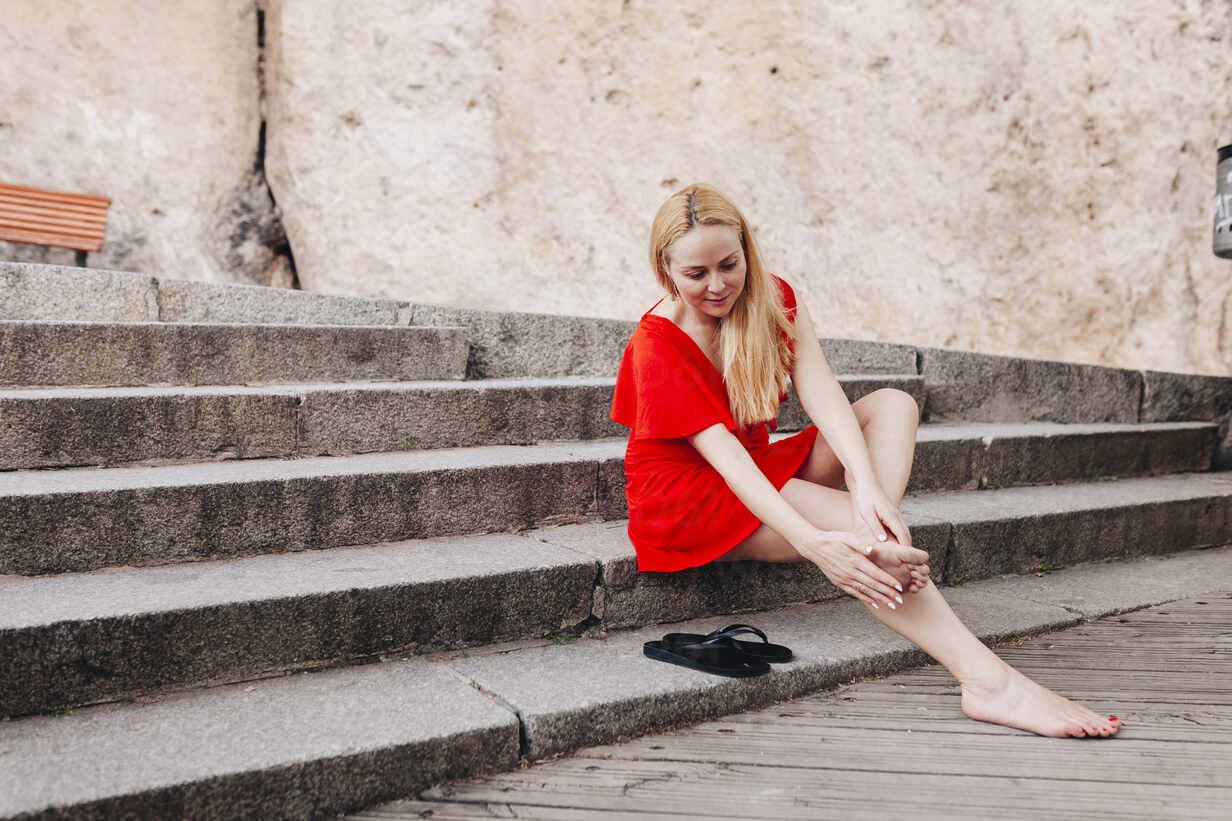 https://images.westend61.de/0001420890pw/woman-wearing-red-dress-sitting-on-steps-and-massaging-her-foot-MRRF00130.jpg