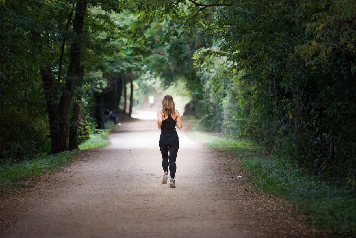 Young Fit Woman Running Away Doing Sport On A Path In Park In A Sunny Day