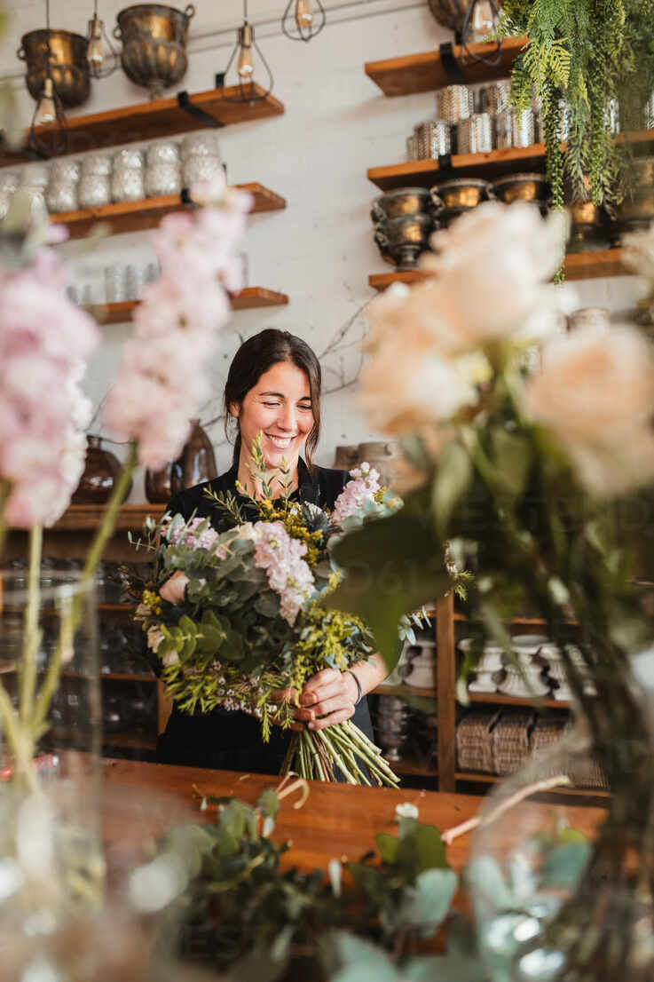 Positive Young Female Floristry Designer With Big Bouquet Of Fresh Blooming Flowers And Green Foliage Standing