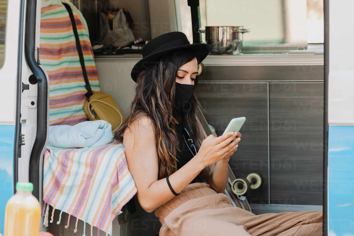 Traveling Female Wearing Protective Mask Sitting In Van And Surfing Internet On Mobile Phone While Resting