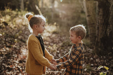Boy And Girl Looking At Each Other While Holding Hands Standing In Forest Stockphoto