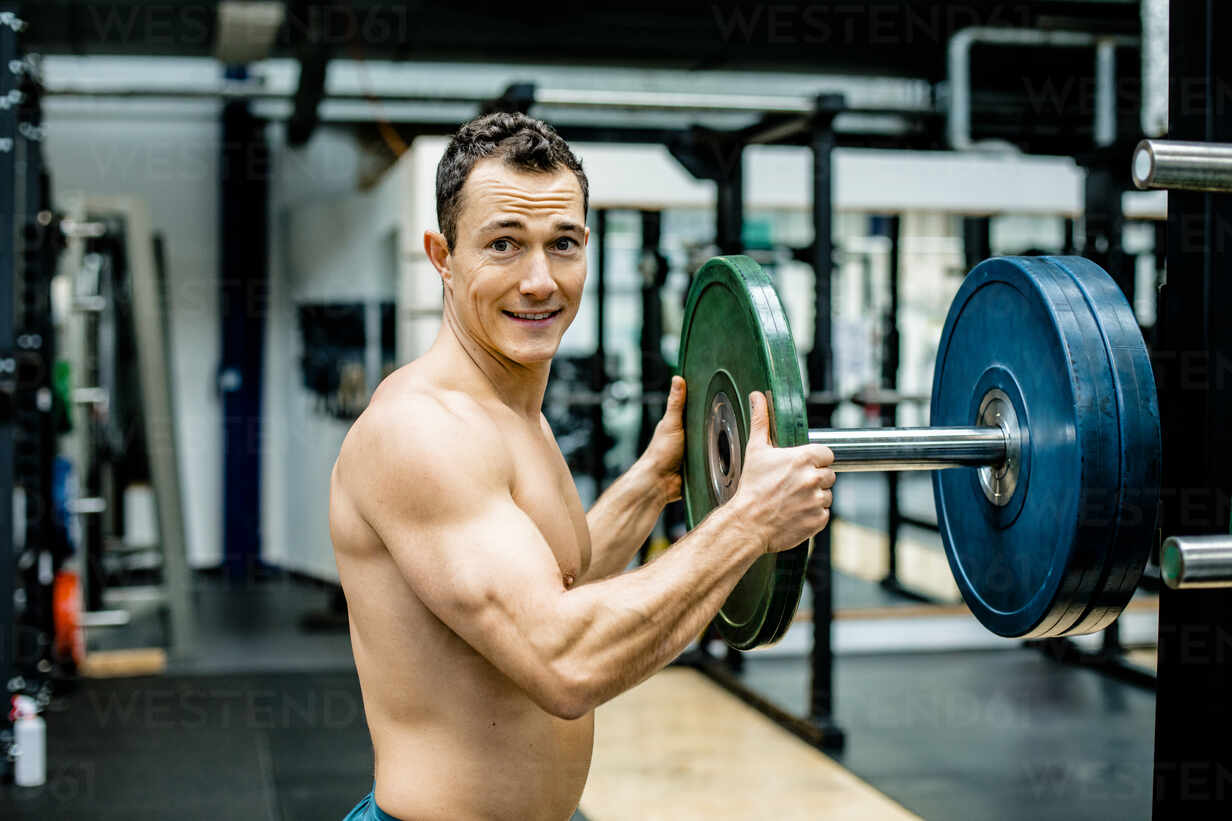 Smiling shirtless athlete holding weights disc in gym - KVF00174 - Katja  Velmans/Westend61